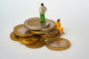 Miniatúrne postavičky ľudí stojace a sediace na kope naskladaných euromincí.