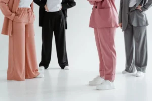 Skupina ľudí v elegantných nohavicových kostýmoch a sakách s bielymi teniskami stojaca v interiéri.