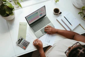 Pohľad zhora na ženu pracujúcu s notebookom, kalkulačkou, finančnými dokumentmi a poznámkovým blokom pri stole