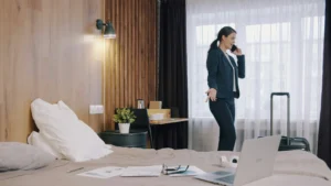 Žena v obleku telefonuje v hotelovej izbe s pripraveným kufrom a notebookom na posteli.