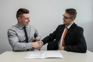 Dvaja muži v košeli a obleku si podávajú ruky nad stolom po úspešnom odoslaní životopisu